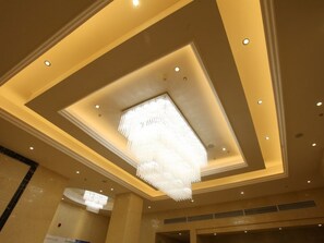 A hotel interior with a modern ceiling design, recessed lighting, and a prominent chandelier.