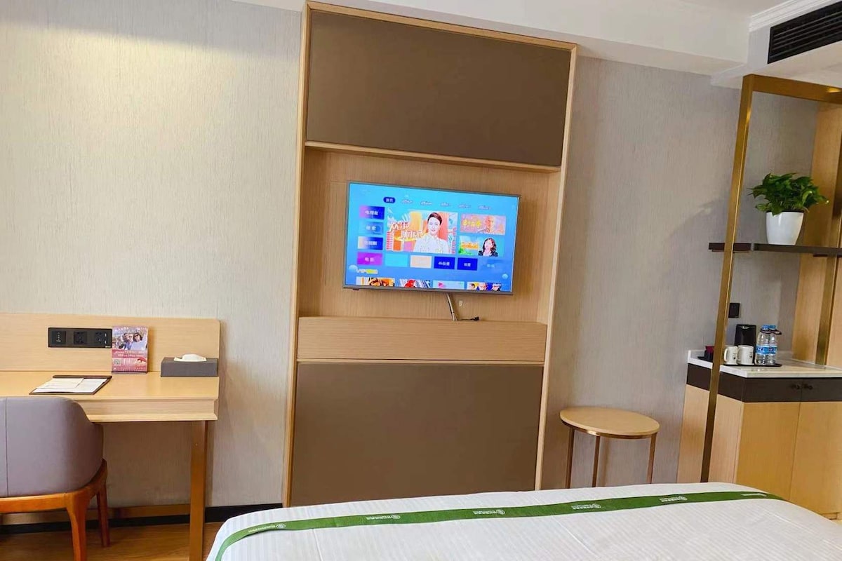 Une chambre d’hôtel équipée d’un lit, d’un bureau, d’une chaise, d’une télévision et d’un petit tabouret.