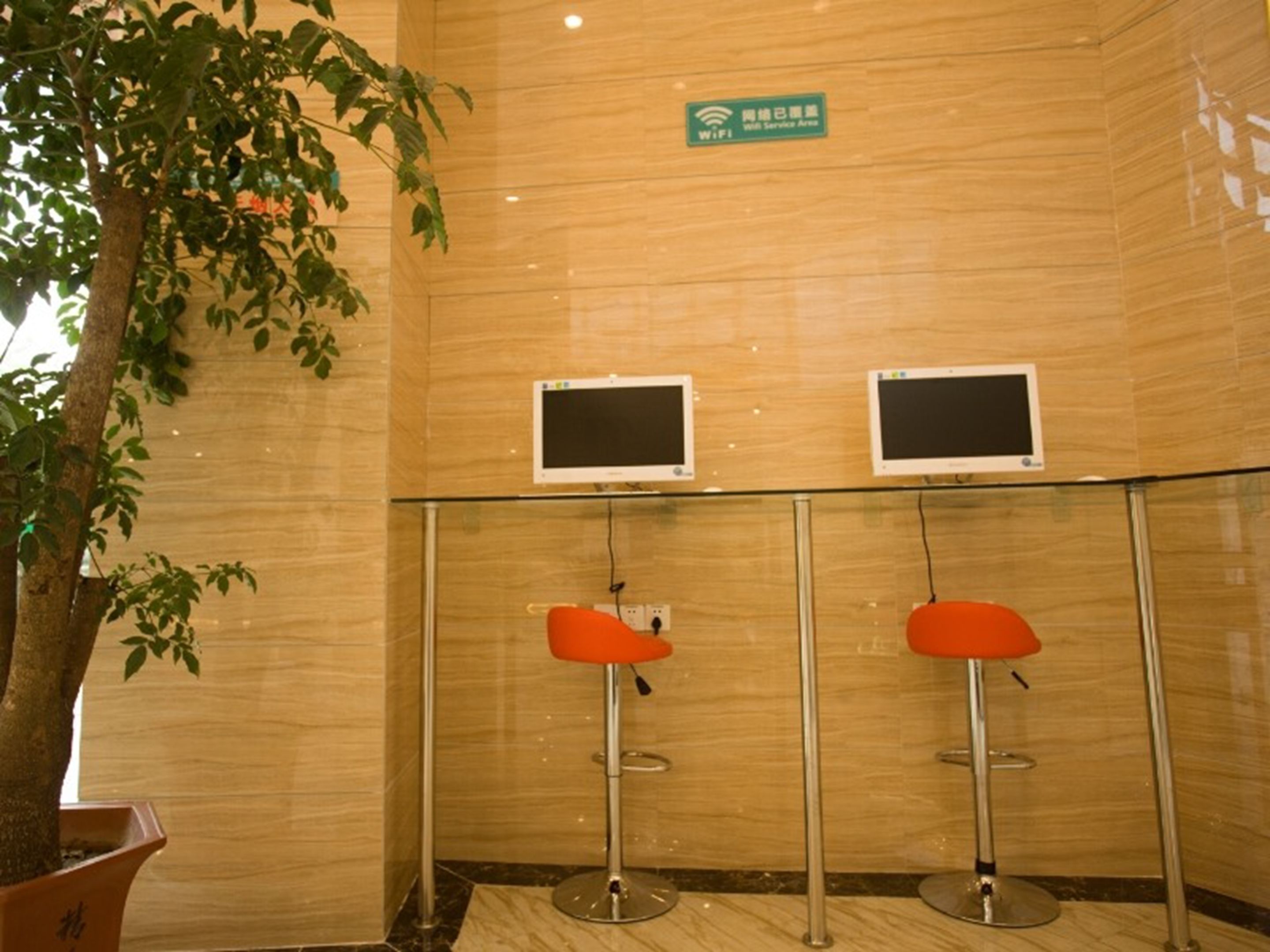 Un área de recepción con dos monitores, un cartel que indica una zona de servicio WiFi y dos sillones naranjas.