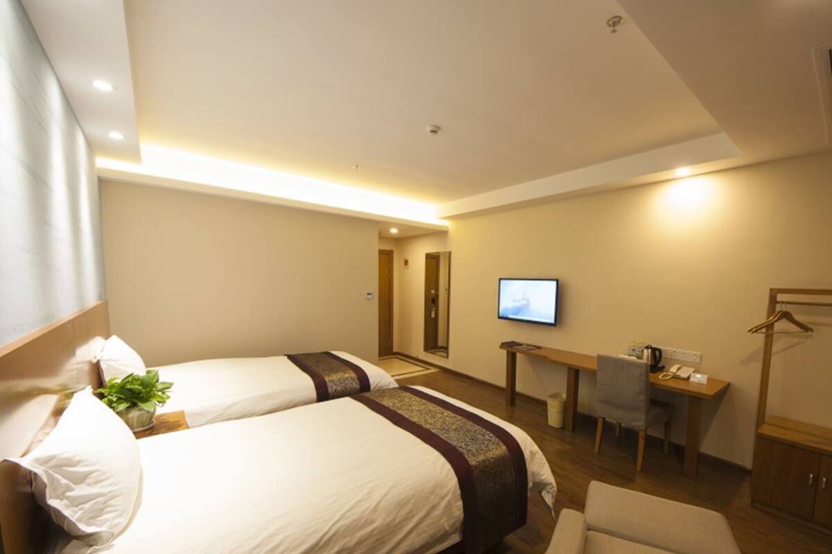 Ein Hotelzimmer mit zwei Betten, einem Schreibtisch, einem Sessel, einem Fernseher und einem Kleiderhaken.