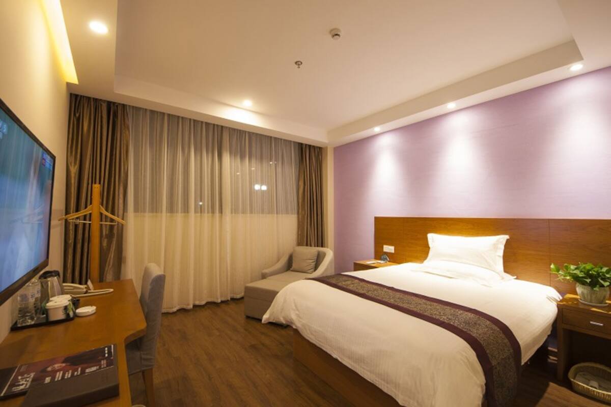 Ein Hotelzimmer mit einem großen Bett, einem Schreibtisch mit Fernseher, einem Sessel und einem Fenster mit Vorhängen.