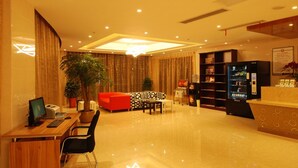 A hotel lobby with a reception desk, a red sofa, a coffee machine, a computer, and a bookshelf. - GreenTree Inn TaiZhou JingJiang ZhongZhou Road Sunshine International Business Hotel (Taizhou)
