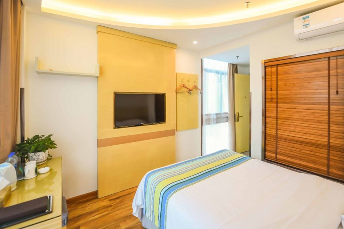 Ein Hotelzimmer mit einem Bett, einem Schreibtisch mit Pflanze, einem Fernseher und einem Kleiderschrank.