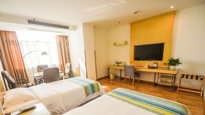 A hotel room with two beds, a desk, a chair, a TV, and a small plant.