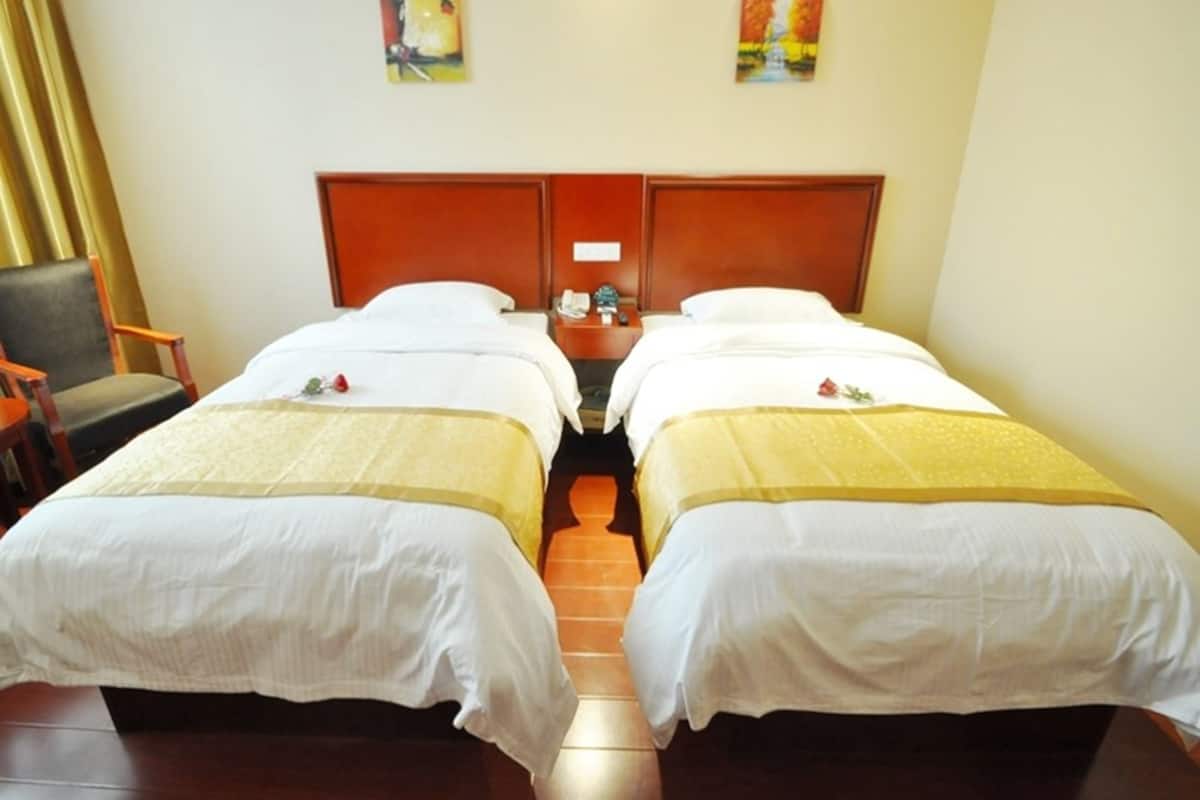 A hotel room with two single beds, wooden headboards, a nightstand with a phone, and a chair.