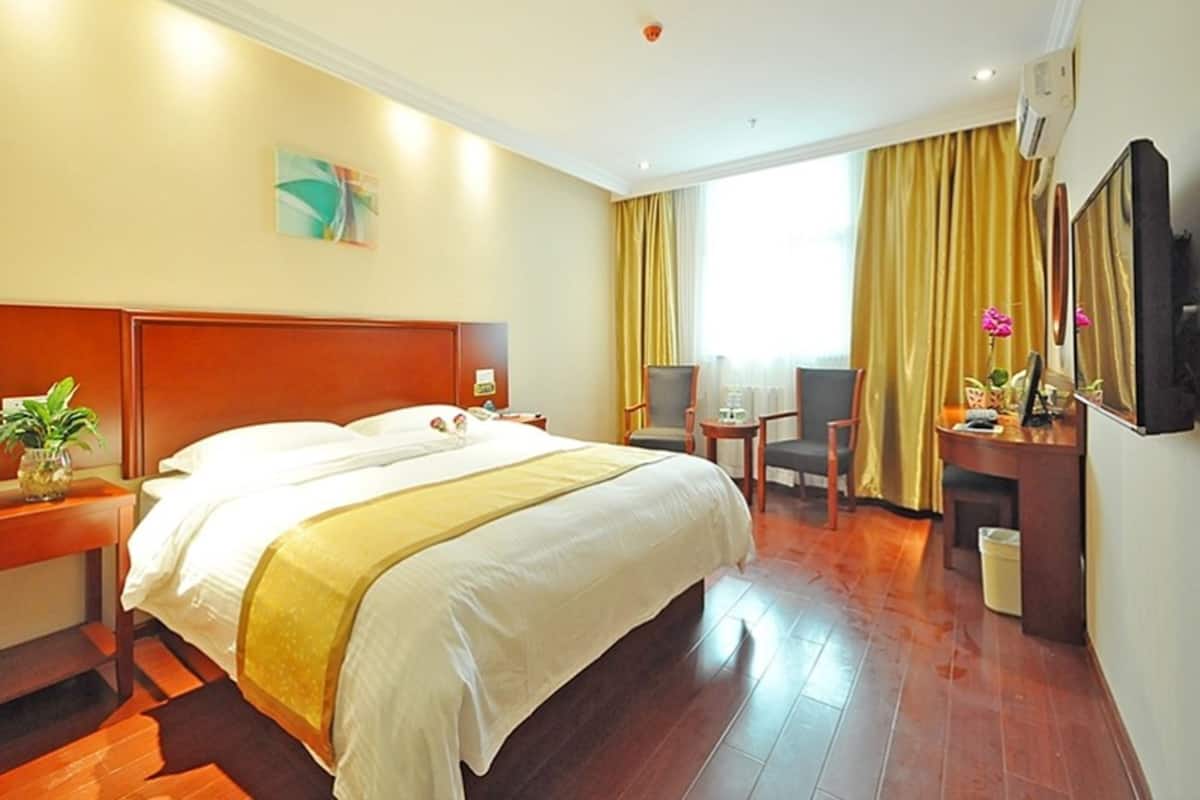 A hotel room with a large bed, a desk with a chair, a small table, and a TV.