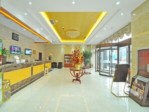 A hotel lobby with a reception desk, a seating area with a vase of flowers, and a glass door entrance. - GreenTree Inn Linyi International Convention Center Express Hotel (Linyi)