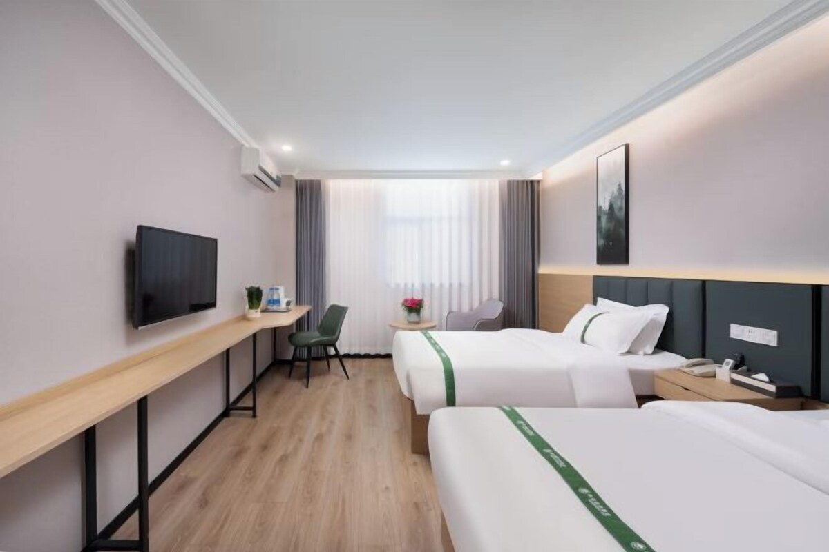 A hotel room with two beds, a desk, a chair, a TV, and a window with curtains.
