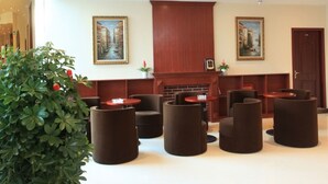 Eine Lobby mit Empfangsschalter, einer Sitzecke mit runden Tischen und Sesseln sowie zwei gerahmten Bildern an den Wänden.