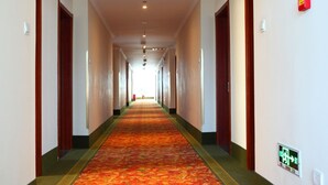 Ein langer, schmaler Hotelkorridor mit rotem Teppich, Holztüren und einer Decke mit eingelassener Beleuchtung.