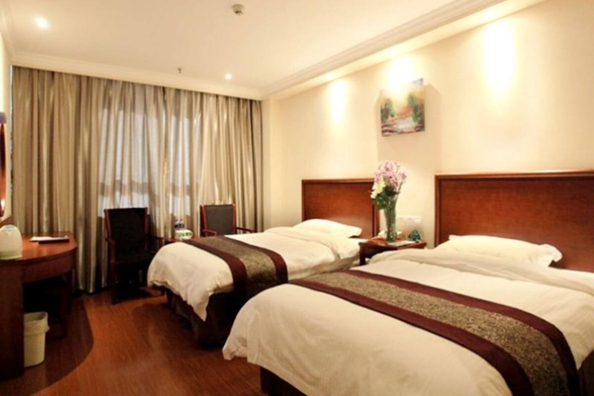 A hotel room with two beds, a desk, a chair, and a large window with curtains.