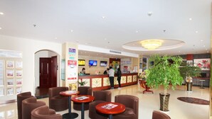 Eine Hotelhalle mit einer Rezeption, mehreren bequemen braunen Sesseln und einer großen Topfpflanze.