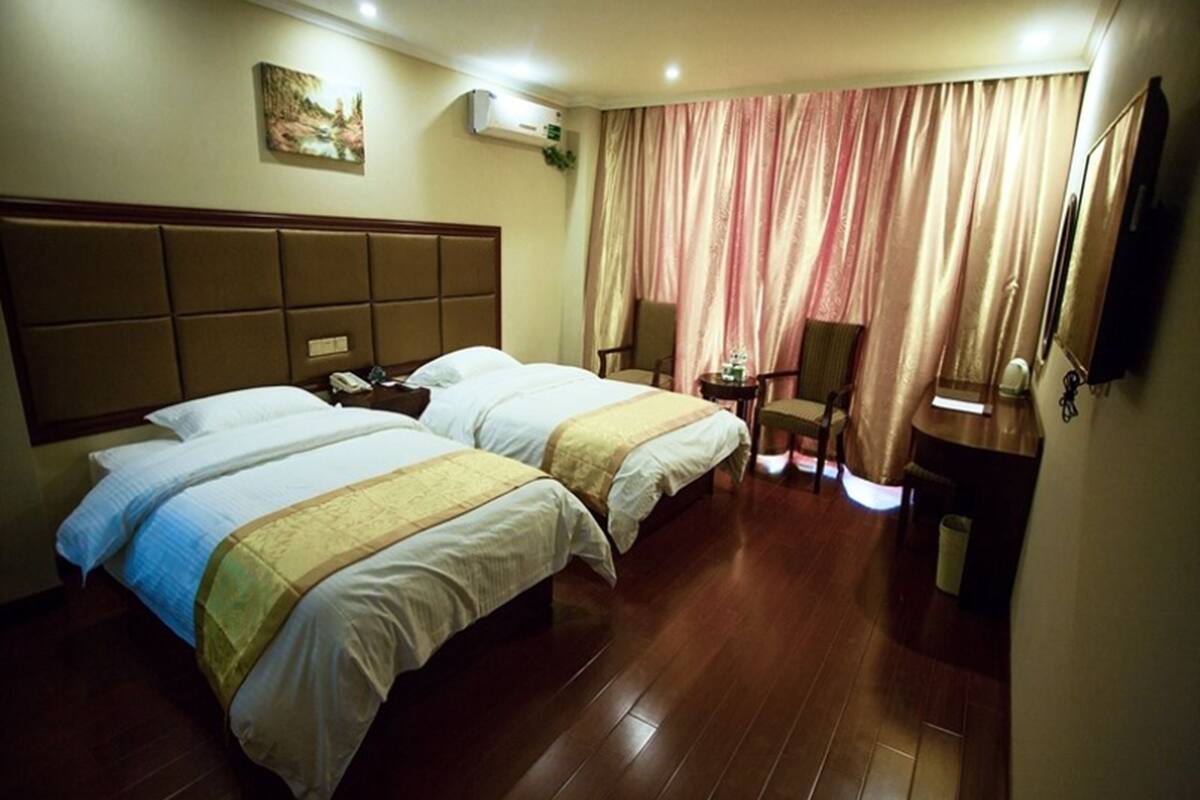A hotel room with two beds, a small desk, a chair, a mirror, and a window with curtains.