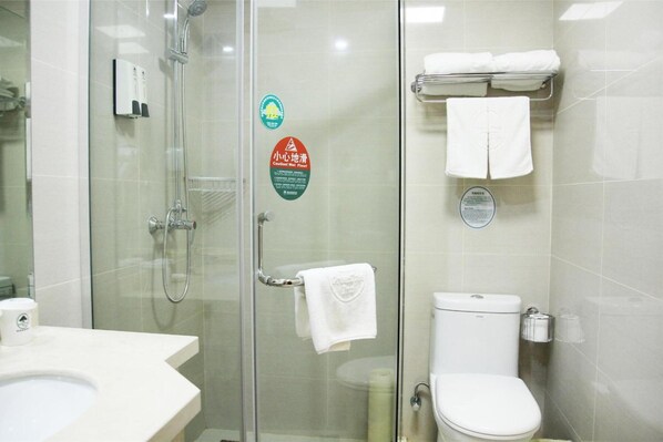 A bathroom with a glass shower enclosure, a toilet, and a sink. There are towels hanging on a rack and a soap dispenser on the wall. - GreenTree Inn ShangQiu Normal College Wenhua W Road Hotel (Shangqiu)
