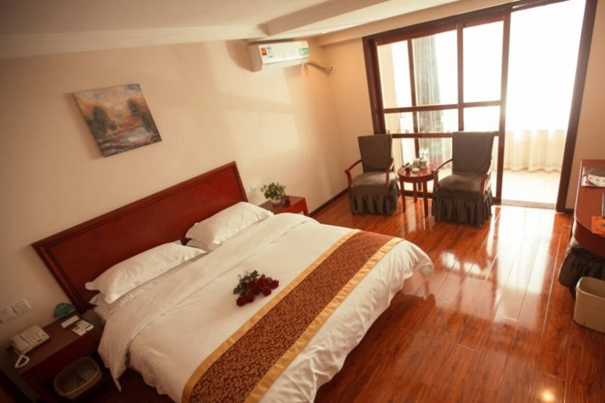 Een hotelkamer met een groot bed, een nachtkastje met telefoon, een kleintje eettafeltje met stoelen en een raam met gordijnen.