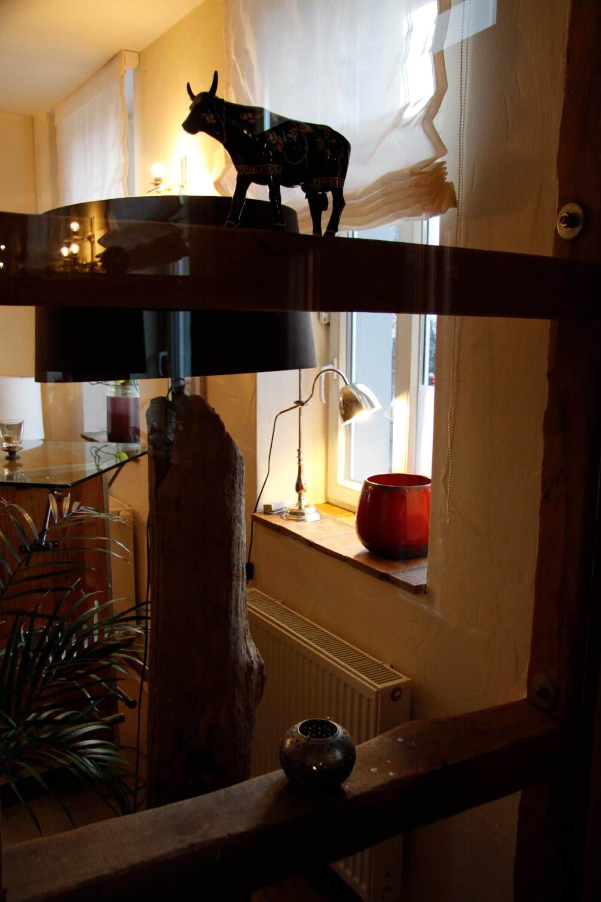 A rustic interior with a wooden beam, a bull figurine, a lamp, and a window with curtains.
