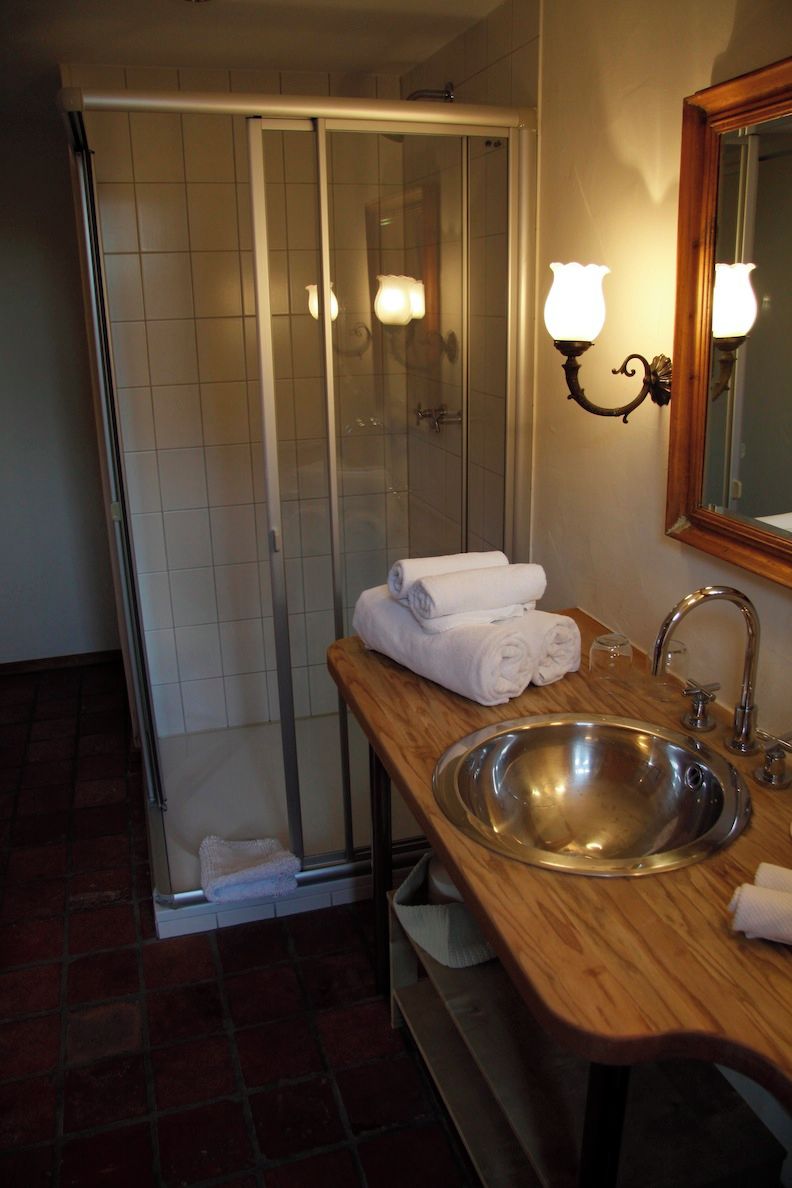 Een badkamer met een glazen douchecabine, een houten wastafelmeubel met een wastafel en een spiegel met wandlampen.