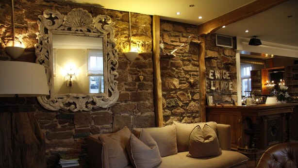 Une pièce chaleureuse avec un mur en pierre, un grand miroir décoratif, un canapé confortable et, au fond, un coin bar.
