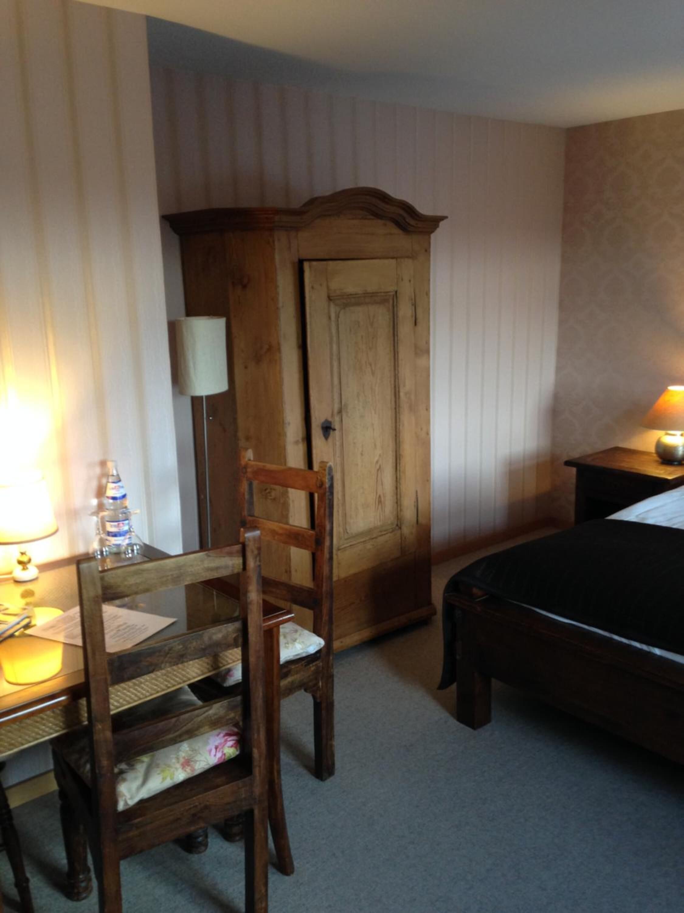 Ein Hotelzimmer mit Holzschrank, Bett, Schreibtisch mit Stuhl und Nachttisch mit Lampe.