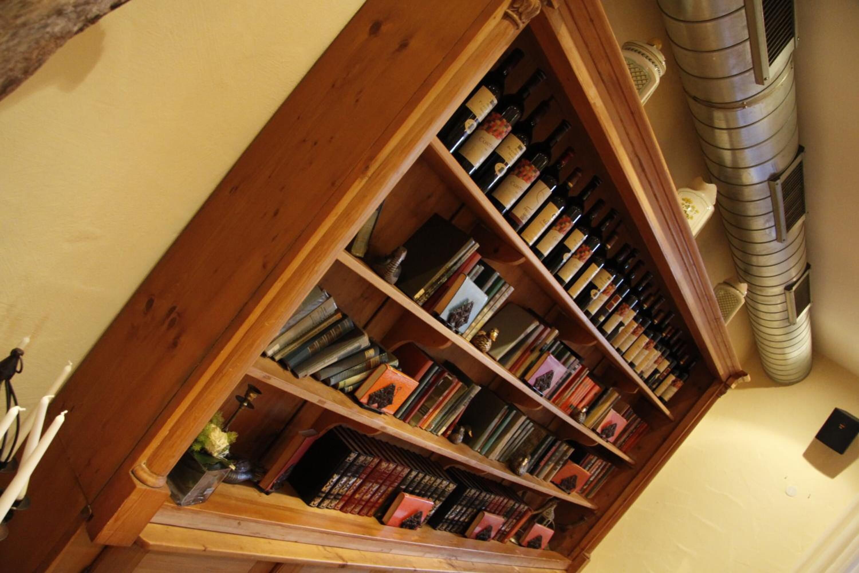 Una estantería de madera llena de libros y botellas de vino.