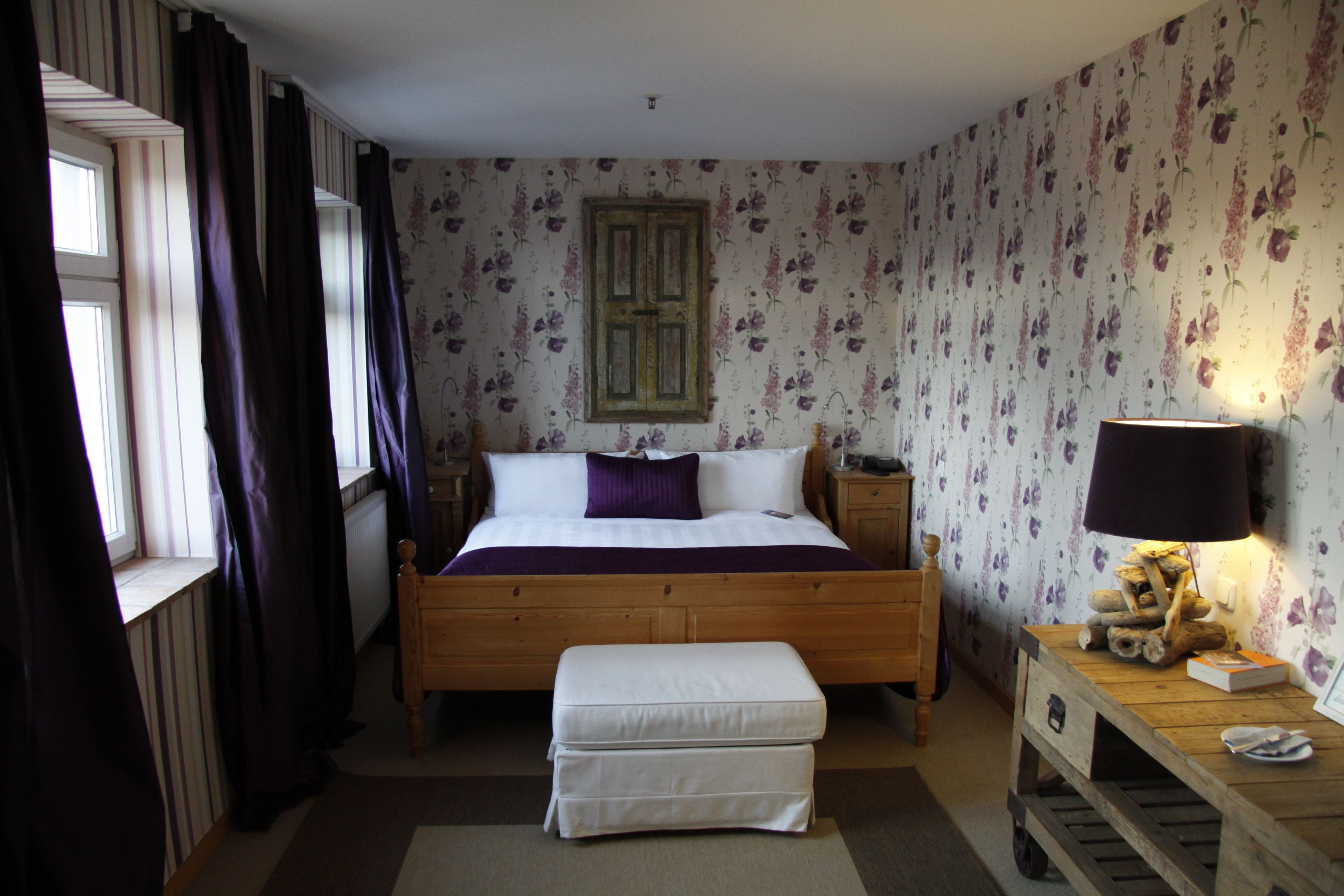 Une chambre à coucher avec un lit en bois, une table de chevet, une lampe et une fenêtre avec des rideaux.