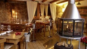 Un coin repas rustique avec des tables et des chaises en bois, des bougies et un poêle à bois central.