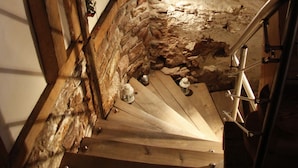 Un escalier étroit, avec des murs en pierre et des poutres en bois, qui mène à un niveau inférieur.