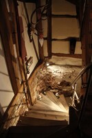 Una escalera estrecha con paredes de piedra y vigas de madera que baja a un nivel inferior.