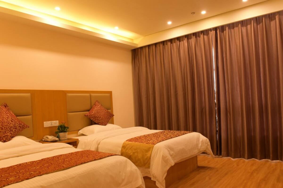 A hotel room with two beds, a wooden headboard, a nightstand with a phone, and a large window with curtains.
