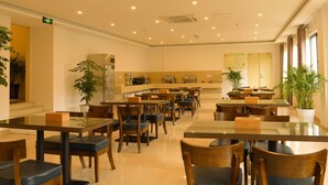 A spacious hotel dining area with multiple tables and chairs, a kitchen in the background, and potted plants. - GreenTree AnHui Wuhu Sanshan Development District Express Hotel (Wuhu)