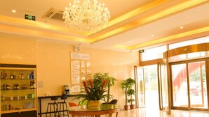A hotel lobby with a glass-top table, chairs, a bar area with shelves of beverages, a chandelier, and potted plants. - GreenTree AnHui Wuhu Sanshan Development District Express Hotel (Wuhu)