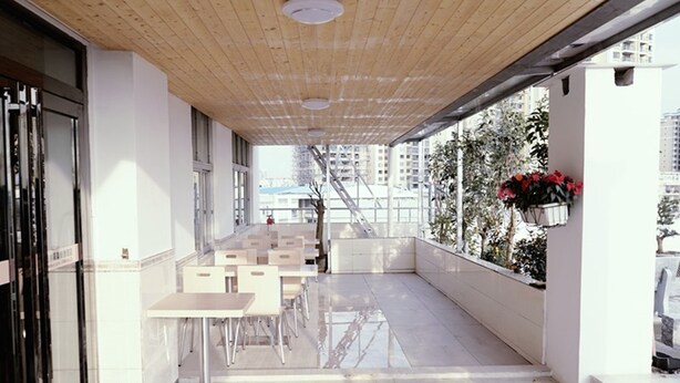 A modern indoor balcony with white tables and chairs, a wooden ceiling, and a view of a cityscape. - GreenTree Inn Beihai HePu County South Huanzhu Road Express Hotel (Beihai)
