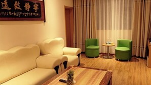A hotel room with a beige sofa, two green armchairs, a wooden coffee table with a pineapple, and a large window with curtains. - GreenTree Inn Beihai HePu County South Huanzhu Road Express Hotel (Beihai)