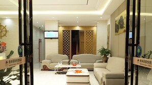 A modern hotel lobby with a reception desk, two sofas, a coffee table, and a TV screen. - GreenTree Inn Beihai HePu County South Huanzhu Road Express Hotel (Beihai)