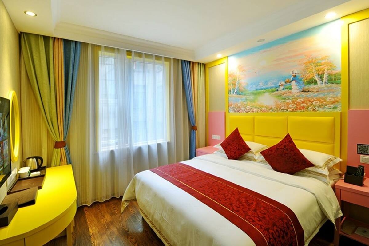 A hotel room with a bed, a desk, a painting on the wall, and a window with curtains.
