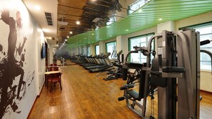 Un gimnasio con cintas de correr, máquinas de pesas y suelo de madera.