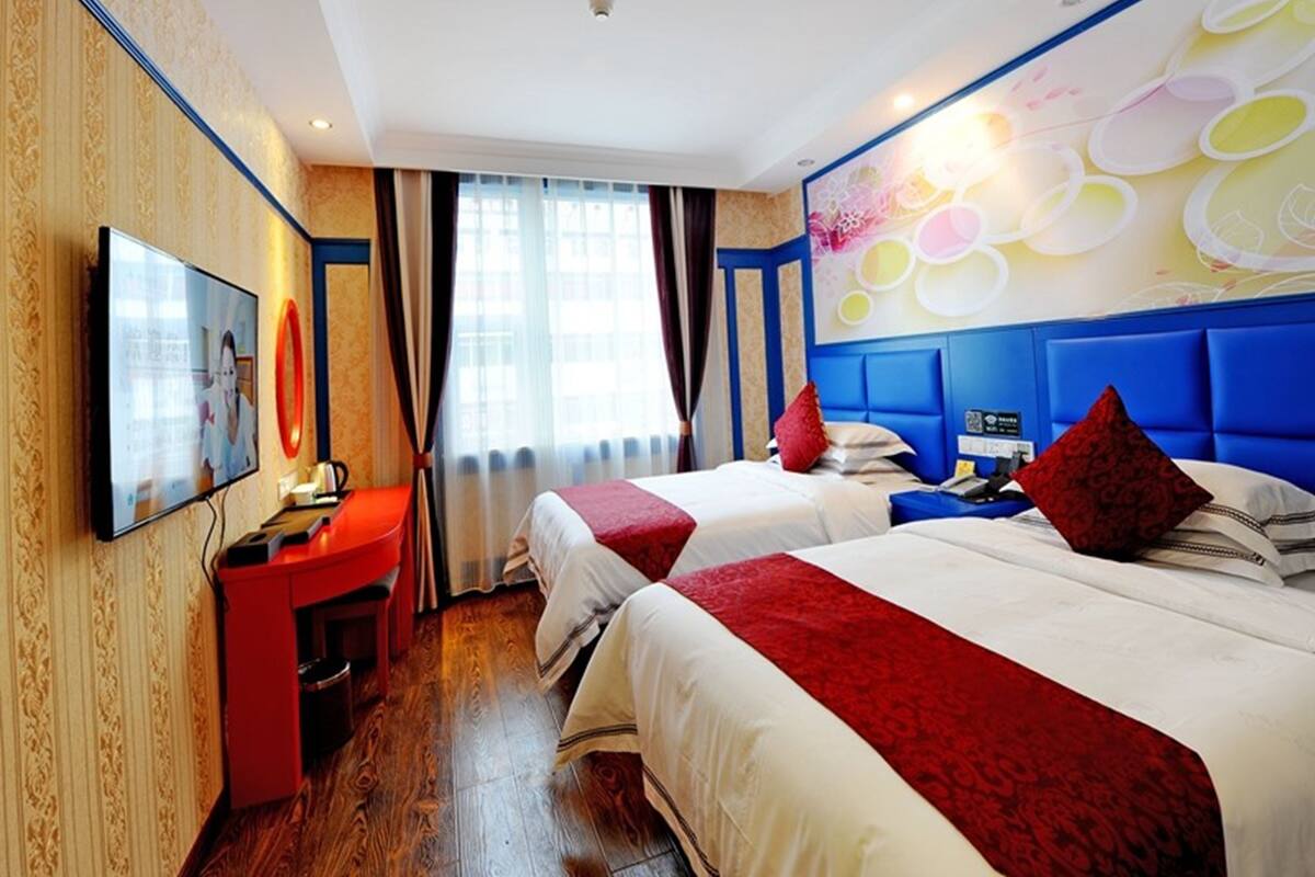 A hotel room with two beds, a TV, a desk, and a large window.