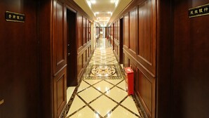 Un pasillo de hotel con puertas de madera, suelo de baldosas y una caja roja a la derecha.