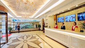 Zona de recepción de hotel con un llamativo diseño floral en el suelo, un candelabro y varias pantallas mostrando contenido.
