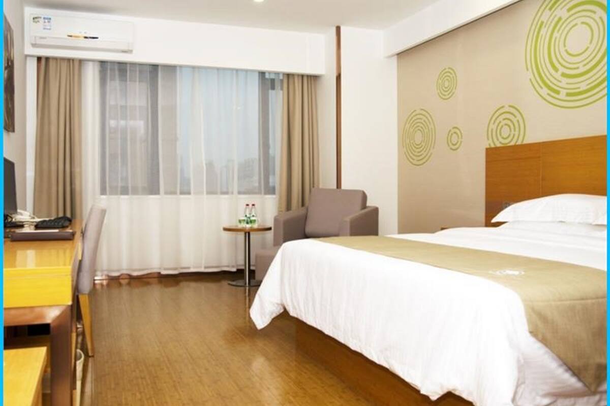 Une chambre d’hôtel avec un grand lit, un bureau avec un ordinateur, une chaise, une petite table avec des boissons et une fenêtre avec des rideaux.