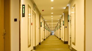 Un couloir d’hôtel avec des portes des deux côtés, chacune étant signalée par une plaque verte indiquant le numéro de la chambre.