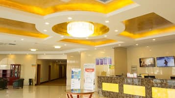 A hotel lobby with a reception desk, a chandelier, and a clean, polished floor.