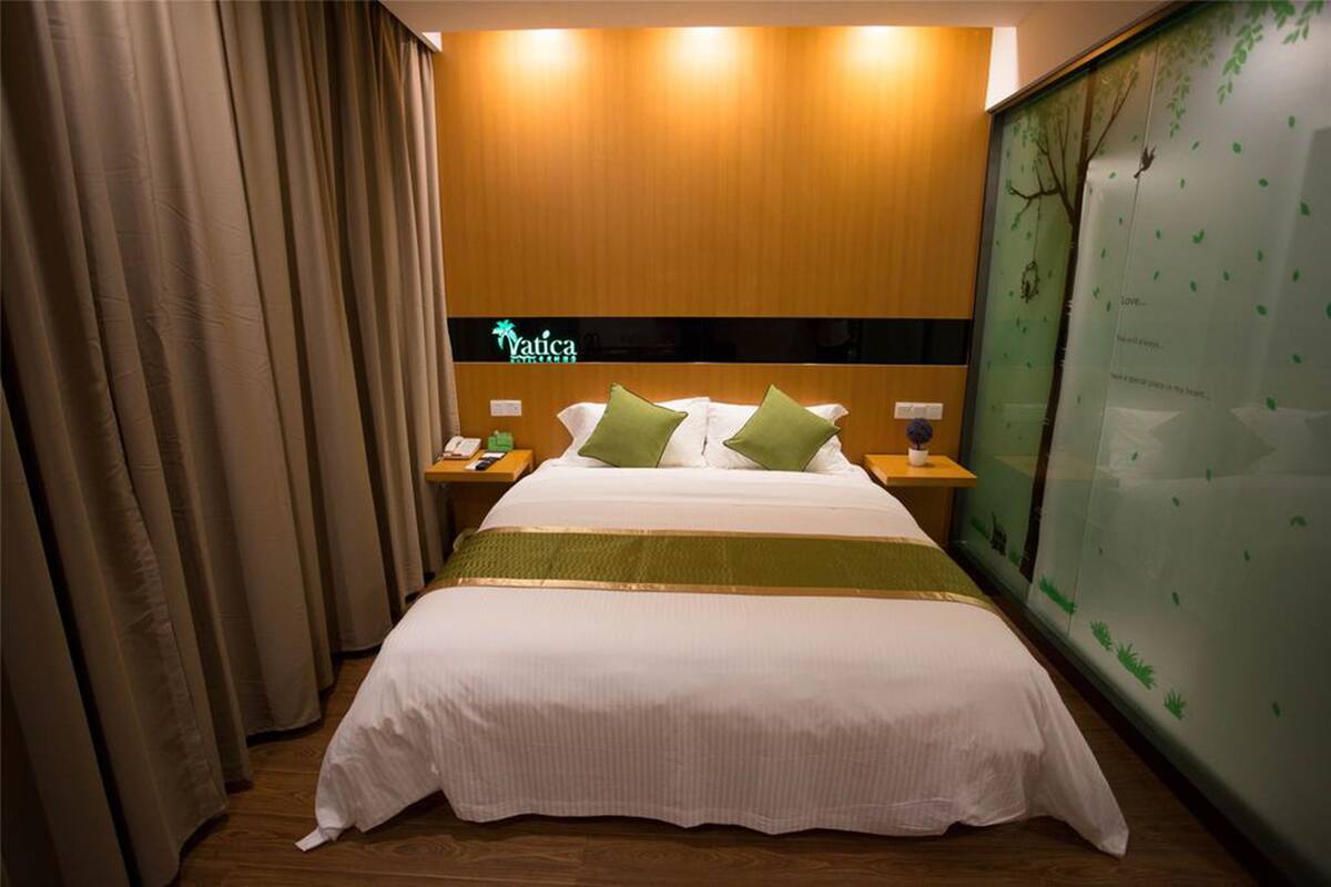 A hotel room with a bed, nightstands, a green wall with a tree decal, and a sign that reads "Yatica."
