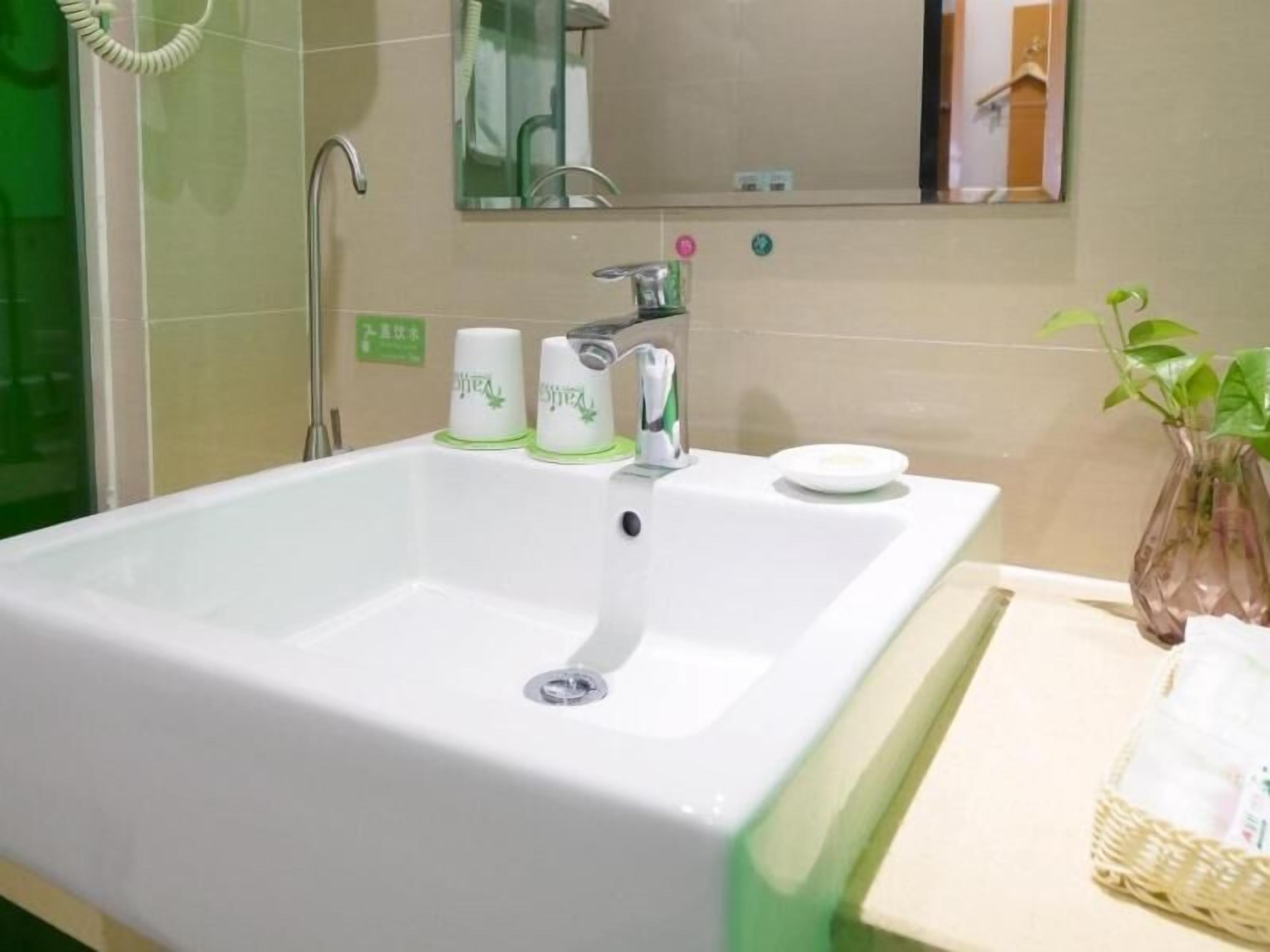Un baño con un lavamanos blanco, un espejo y una planta verde.