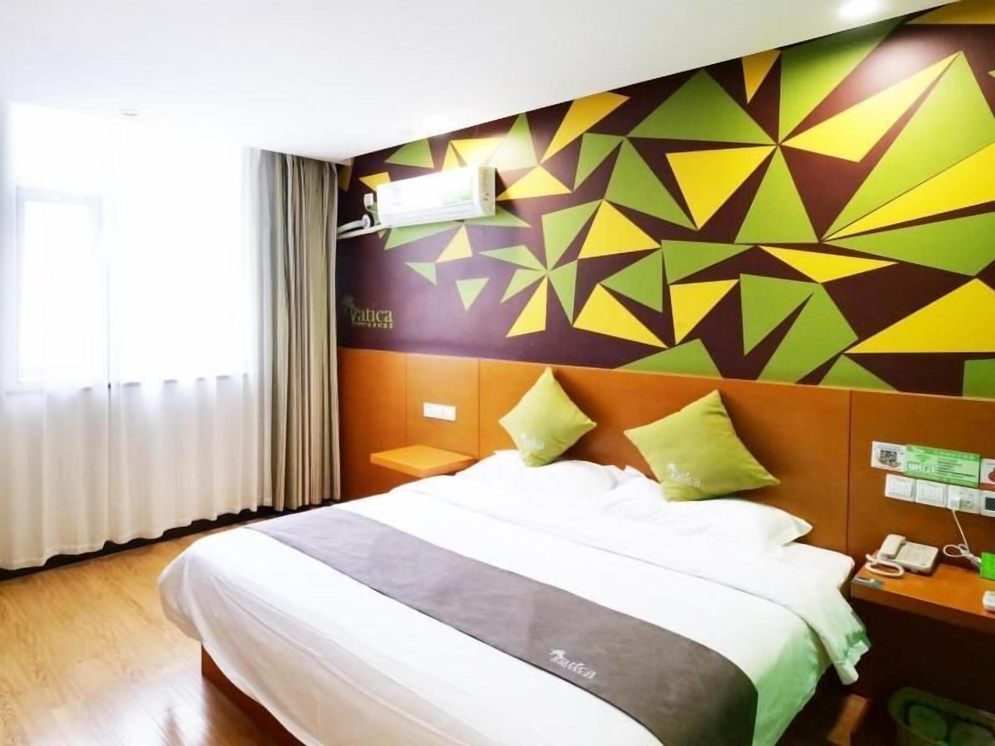 Habitación de hotel con cama, mesita de noche, aire acondicionado instalado en la pared y un muro con estampado geométrico.