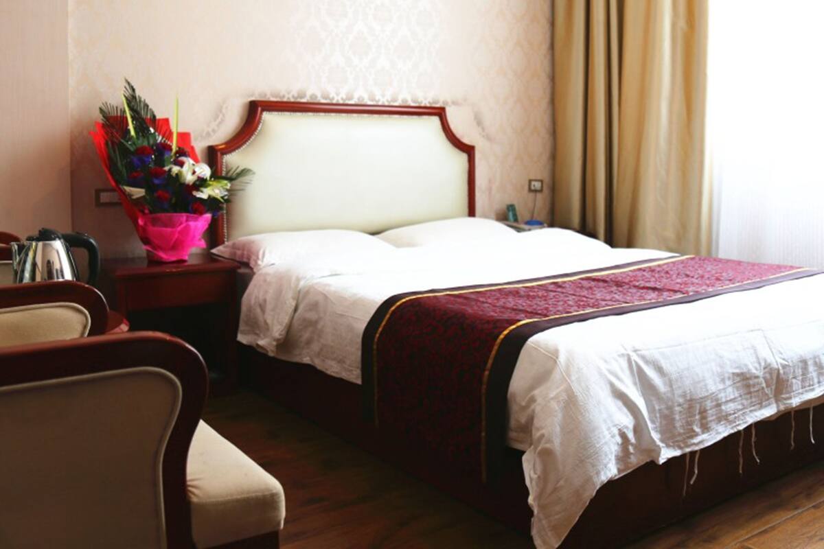 A hotel room with a bed, a nightstand, a chair, and a vase of flowers.