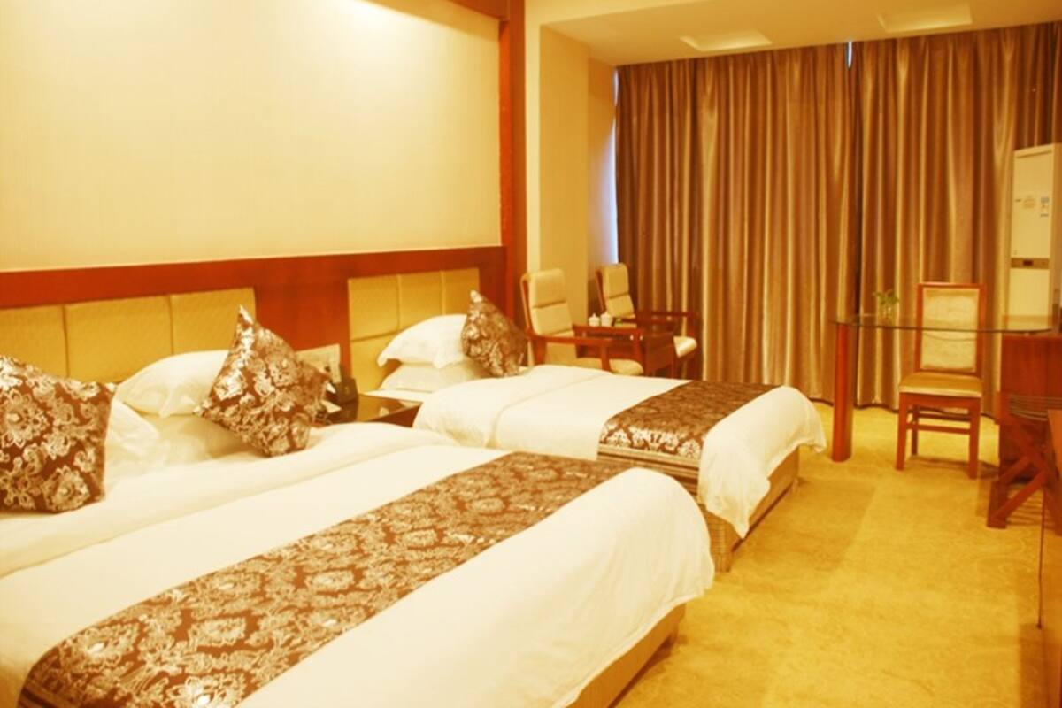 Una habitación de hotel con dos camas, un escritorio, una silla y un ventanal grande con cortinas.