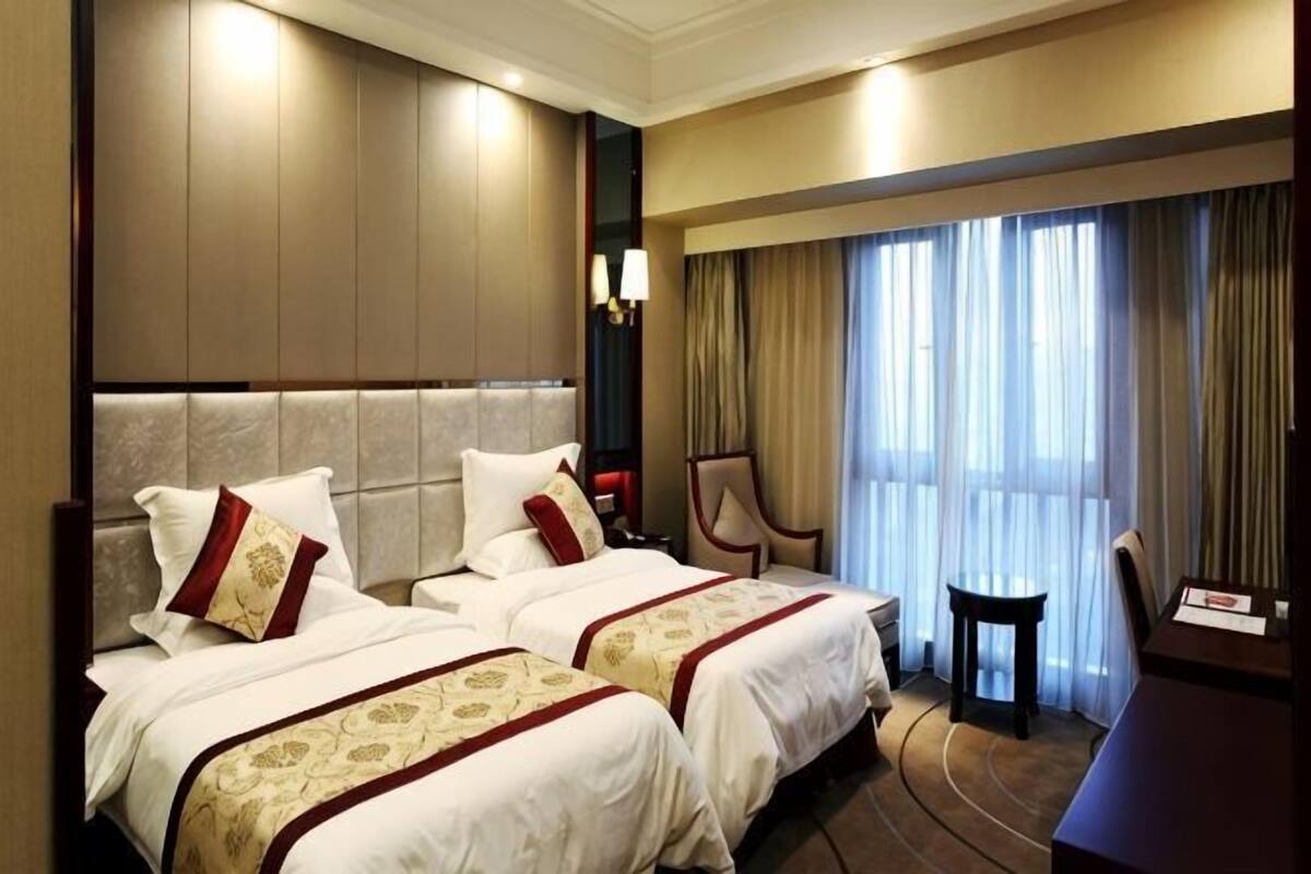 Una habitación de hotel con dos camas, un escritorio, una silla y un ventanal con cortinas.