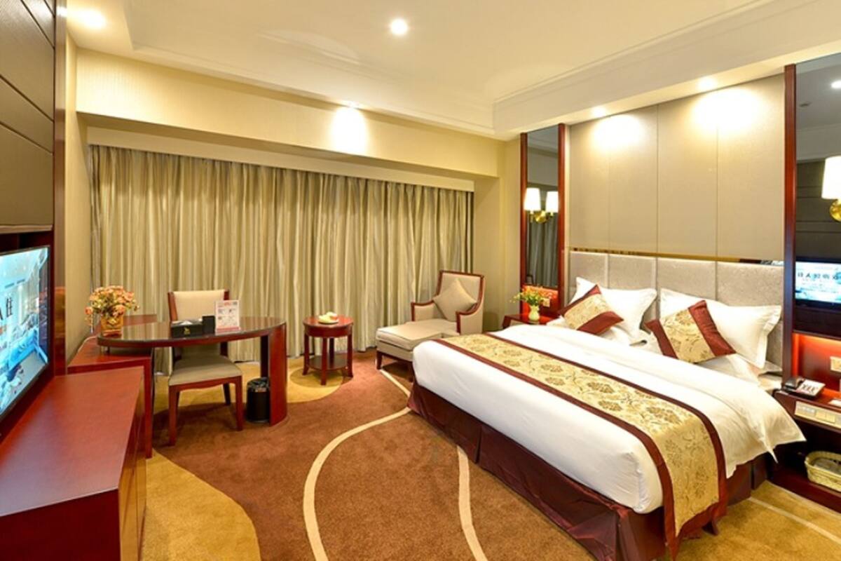 Habitación de hotel con una cama grande, un escritorio con una silla, un televisor y un espejo amplio.