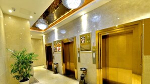 Un vestíbulo de hotel con piso de mármol, una planta en maceta y tres ascensores.